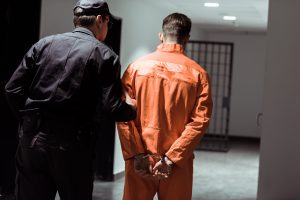 rear view of prison officer leading prisoner in handcuffs in corridor